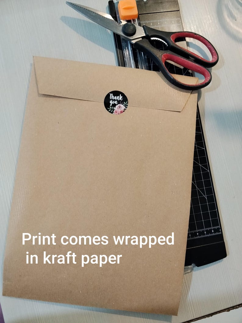 May include: A brown kraft paper envelope sealed with a "Thank You" sticker featuring floral accents. The text "Print comes wrapped in kraft paper" is visible. A pair of scissors and a paper cutter are in the background.