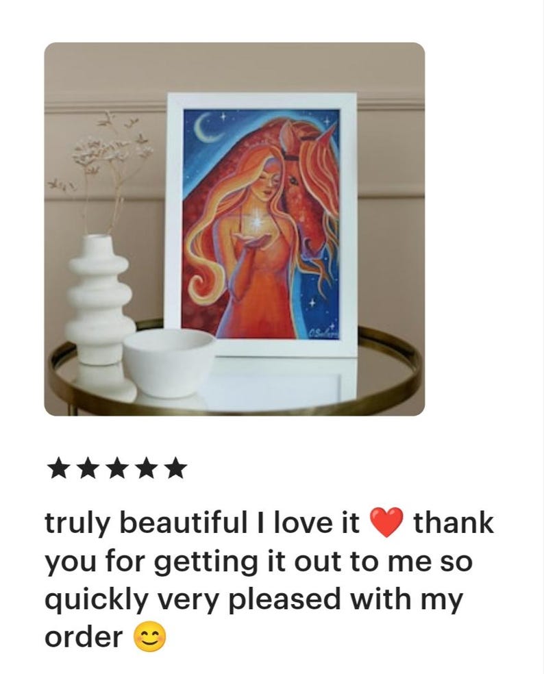 May include: A framed art print featuring a woman with long red hair and a horse, set against a blue starry sky. The woman holds a glowing object. The artwork is displayed on a table with a white vase and bowl.
