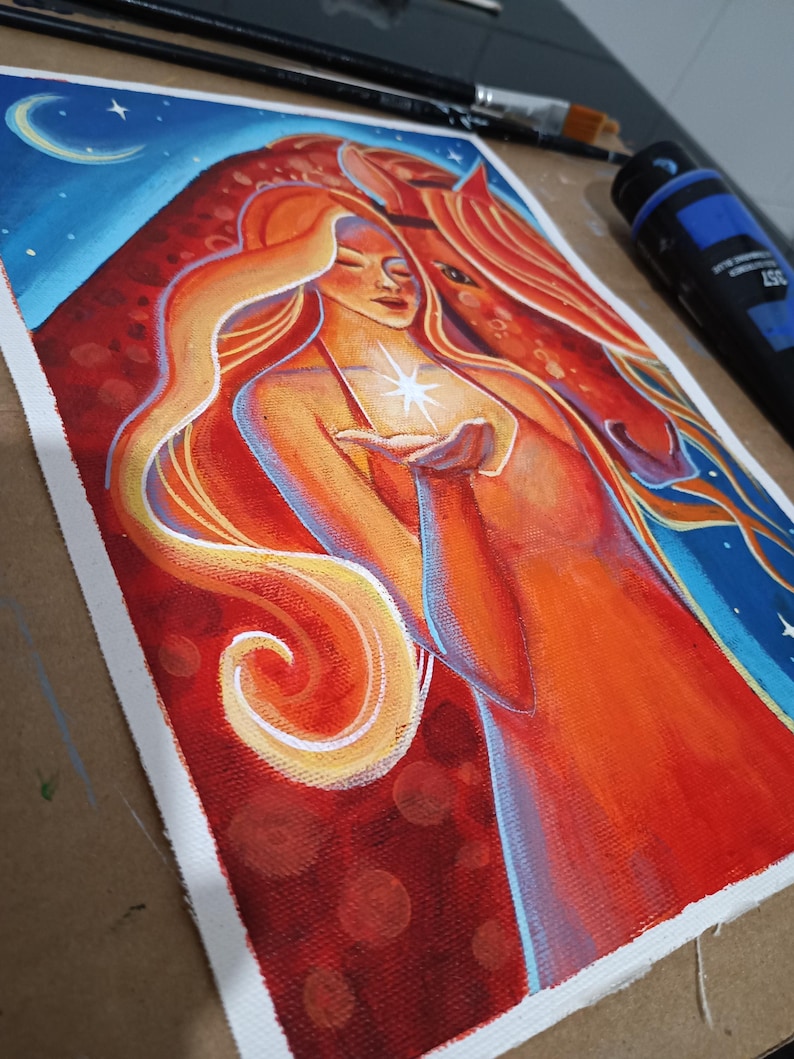 May include: An acrylic painting on canvas depicts a woman with long orange hair and a horse. The woman holds a glowing star. The background features a blue sky with a crescent moon and stars. The artwork uses warm colors like red, orange, and yellow.