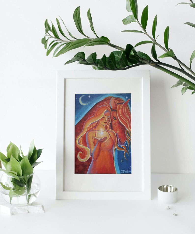 May include: A framed art print featuring a woman with long, flowing red hair holding a glowing star, alongside a red horse. The background shows a starry night sky with a crescent moon. The artwork is in a white frame.