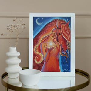 May include: A framed painting depicts a woman with long, flowing orange hair holding a glowing star, alongside a red horse. The background features a blue night sky with a crescent moon and stars. The artwork is in a white frame.
