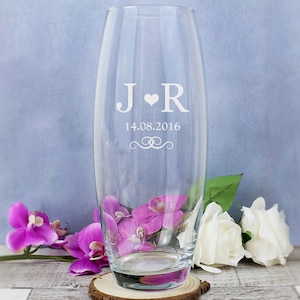 May include: A clear glass vase with a personalised inscription. The inscription reads "J ♥ R 14.08.2016" with a decorative swirl design. The vase is sitting on a wooden base.