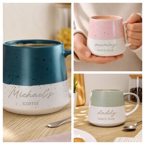 May include: Three ceramic mugs with a two-tone speckled design. One dark blue mug reads Michael's COFFEE. One pink mug reads mummy SINCE 2026. One sage green mug reads daddy SINCE 2026. Each mug features a white base and a colored top section.