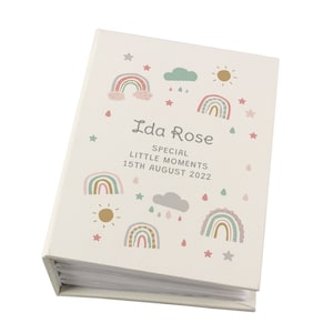 May include: A white photo album with a rainbow, cloud, and sun design. The album has the text "Ida Rose Special Little Moments 15th August 2022" printed on the front.