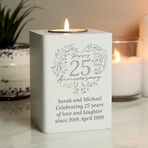 May include: White square candle holder with a silver heart design and the text "Happy 25th Anniversary". The text below the heart reads "Sarah and Michael Celebrating 25 years of love and laughter since 20th April 1999".