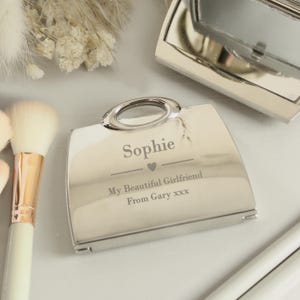 May include: A silver compact mirror with a handbag design. The mirror is engraved with the name "Sophie", the text "My Beautiful Girlfriend", and "From Gary xxx".