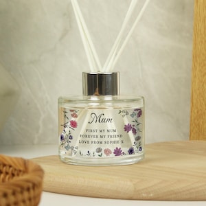 May include: A clear glass diffuser bottle with a silver cap and floral design. The bottle has a label that reads "Mum First My Mum Forever My Friend Love From Sophie X".