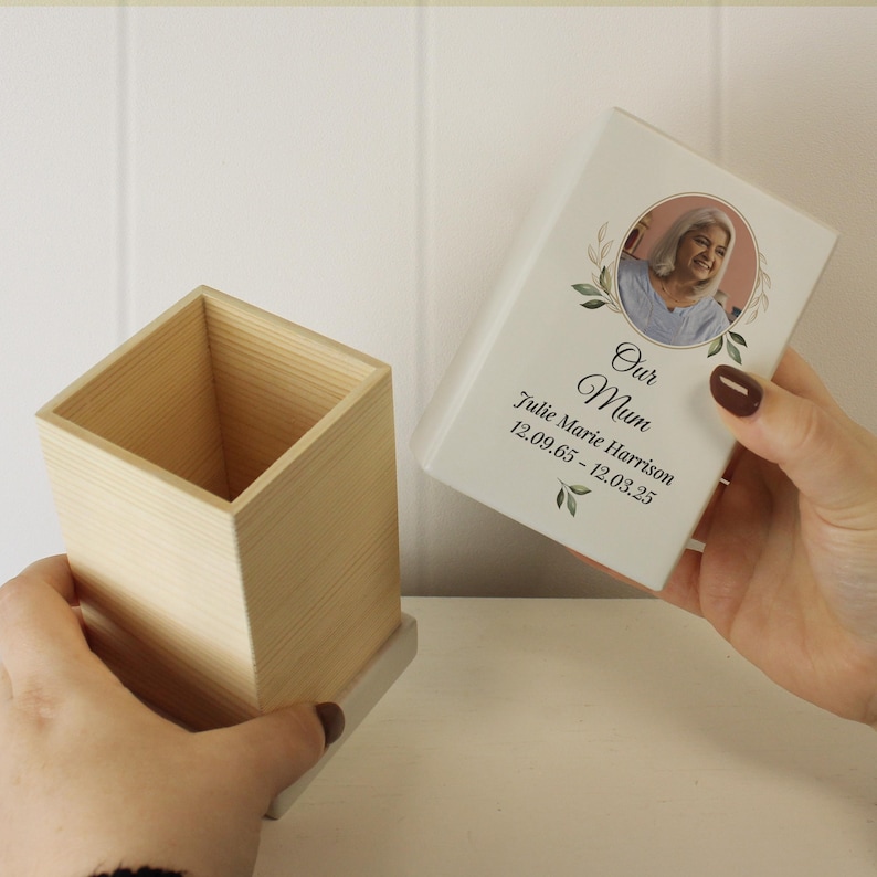 May include: A white wooden box with a lid. The lid has a photo of a woman with a floral design and the text "Our Mum Julie Marie Harrison 12.09.65 - 12.03.25".