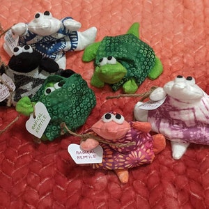 May include: Five plush toys shaped like different animals, including a turtle, a crab, a frog, and two other creatures. Each toy is wrapped in a colorful fabric with a heart-shaped tag that reads "Radical Reptile".