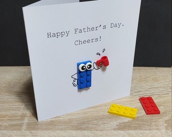 Cheers! Birthday Card (or any occasion) with genuine LEGO® pieces, with a brick-person holding a cup and saying "Cheers!"