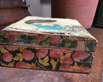 May include: A rectangular wooden box featuring a decorative paper overlay with a vintage illustration of a person on the lid and a pattern of pink hydrangea flowers on a dark green background covering the sides, showing signs of wear.