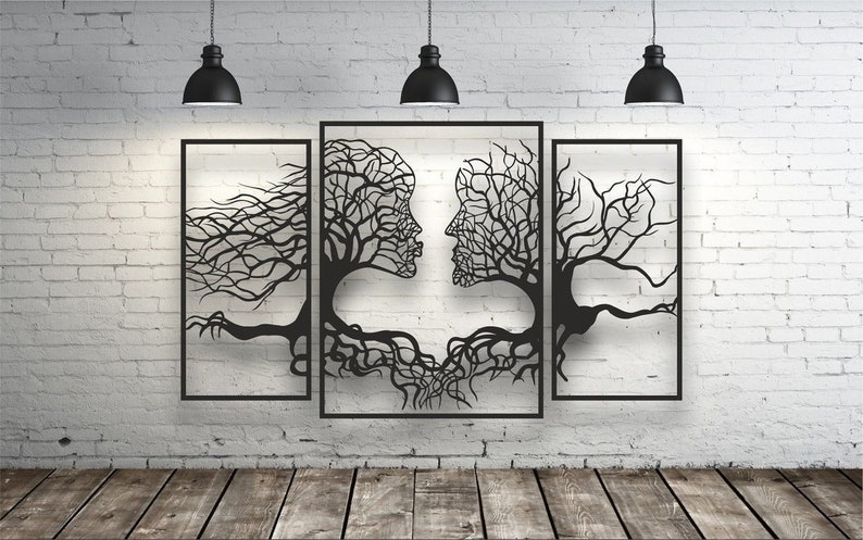 May include: Black metal wall art depicting two faces formed by tree branches and roots. The artwork is composed of three framed panels, mounted on a white brick wall. Three black pendant lights hang above the artwork.
