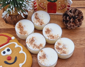 May include: Six unscented white tea light candles with a cinnamon scent. The candles are arranged in a circle on a wooden surface.
