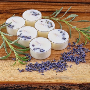 May include: Six white tea light candles with dried lavender flowers on a wooden surface. The candles are arranged in a circle with lavender flowers scattered around them.
