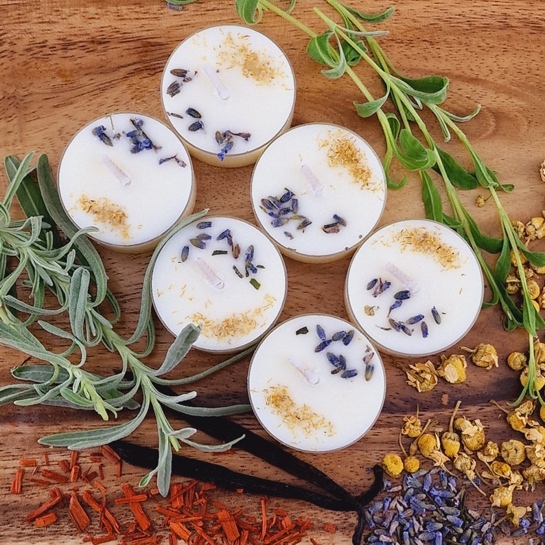 May include: Six white tea light candles with dried lavender and chamomile flowers on a wooden surface.