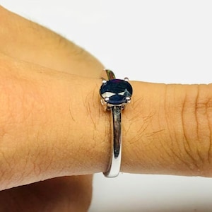 May include: A silver ring with a dark blue oval gemstone set in a prong setting.