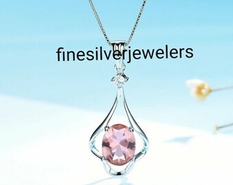 May include: A silver necklace with a pink gemstone pendant. The pendant is set in a delicate silver frame with a small diamond accent. The necklace is on a white background.