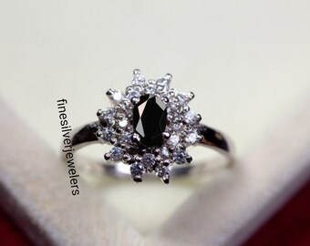May include: A silver ring with a black oval gemstone surrounded by smaller white gemstones. The ring is set in a flower-like design.