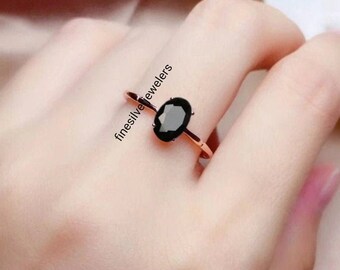 May include: A rose gold ring with a black oval gemstone. The ring is on a person's finger.