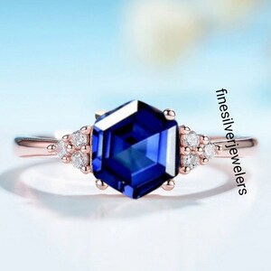 May include: A rose gold ring with a large, hexagonal, blue sapphire gemstone surrounded by smaller, round, white diamonds.