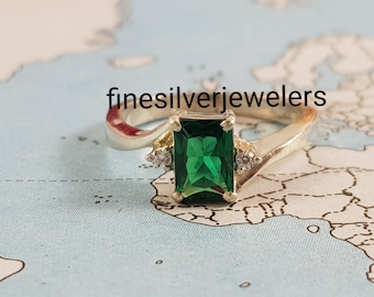 May include: A silver ring with a green emerald gemstone and two smaller clear gemstones. The ring is on a map background.