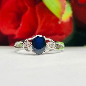 May include: A silver ring with a large oval blue gemstone and two smaller clear gemstones on either side.