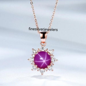 May include: A rose gold necklace featuring a star ruby pendant encircled by clear cubic zirconia stones. The pendant is shaped like a flower.
