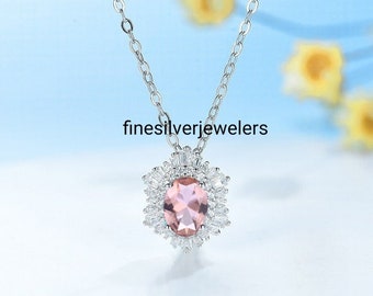 May include: A silver chain necklace with a pink oval gemstone surrounded by smaller clear gemstones in a floral design. The pendant is attached to a silver chain.