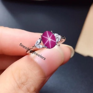 May include: A silver ring with a pink star ruby gemstone and small white diamonds. The ring is set in a leaf design.