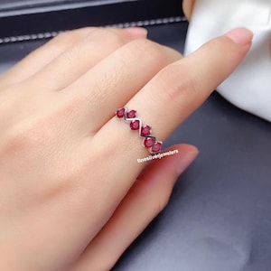 May include: A silver ring with a zig-zag pattern of red gemstones. The ring is on a person's finger.