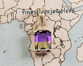 Può includere: Un ciondolo con una pietra preziosa ametrino rettangolare con una sfumatura di viola e giallo, incastonata in una montatura in metallo argentato con una piccola pietra chiara come accento. Il testo finesilverjewelers è visibile sopra il ciondolo.