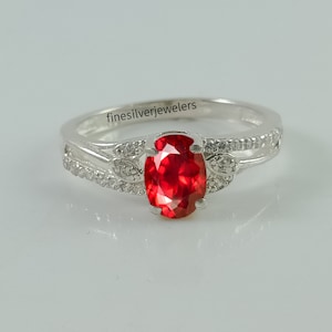 May include: A silver ring with a red oval gemstone and small clear stones set in the band. The ring is inscribed with the text "finesilverejewelers".