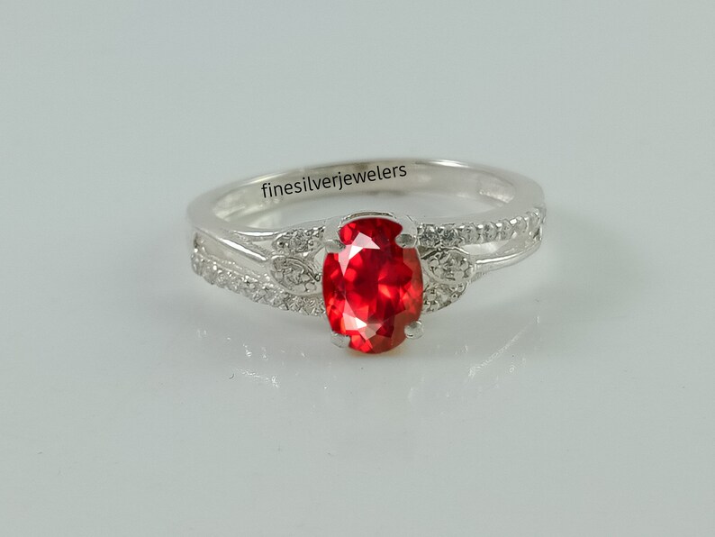 May include: A silver ring with a red oval gemstone and small clear stones set in the band. The ring is inscribed with the text "finesilverejewelers".