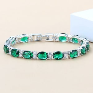 May include: A silver bracelet with a row of oval-shaped green gemstones and smaller clear gemstones.