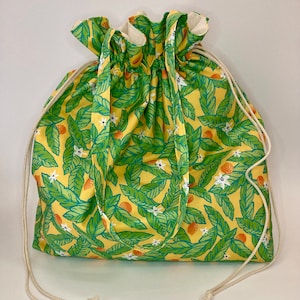 May include: A yellow drawstring bag with a green and white floral pattern featuring small orange fruits. The bag has a long handle and is made of cotton fabric.