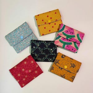 Peut inclure: Six pochettes rectangulaires en tissu avec fermetures à pression, présentant divers motifs dont un jaune à pois avec des fleurs rouges, un imprimé floral bleu clair, un motif de tranches de pastèque rose, un imprimé botanique bleu marine, un motif de vigne rouge et un imprimé floral jaune moutarde.