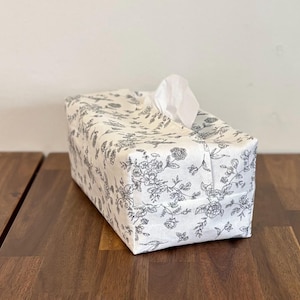 May include: White tissue box cover with a black floral pattern. The cover is made of fabric and has a square shape.