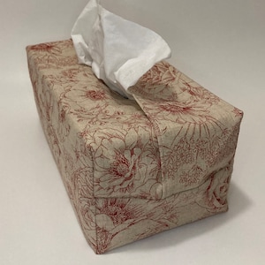 Könnte beinhalten: Ein beigefarbener Tissuebox-Bezug mit rotem Blumenmuster. Der Bezug ist aus Leinen und hat eine quadratische Form.