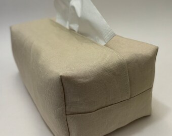 May include: A beige linen tissue box cover with a white tissue box inside. The cover has a simple design and is made of a soft, natural fabric.