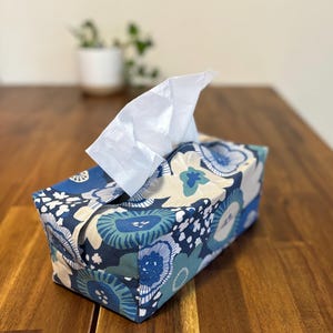 May include: A blue and white floral tissue box cover with a white tissue box inside. The tissue box cover is made of fabric and has a rectangular shape.