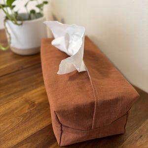 May include: A brown linen tissue box cover with a white tissue box inside.
