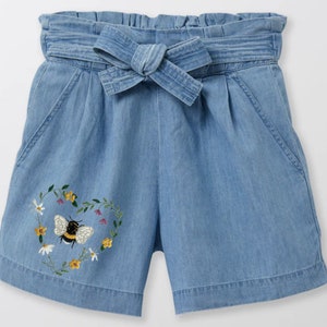 Peut inclure: Short en jean bleu clair &agrave; taille haute avec une ceinture &agrave; nouer. Le short est orn&eacute; d'un motif brod&eacute; en forme de c&oelig;ur avec une abeille et des fleurs.