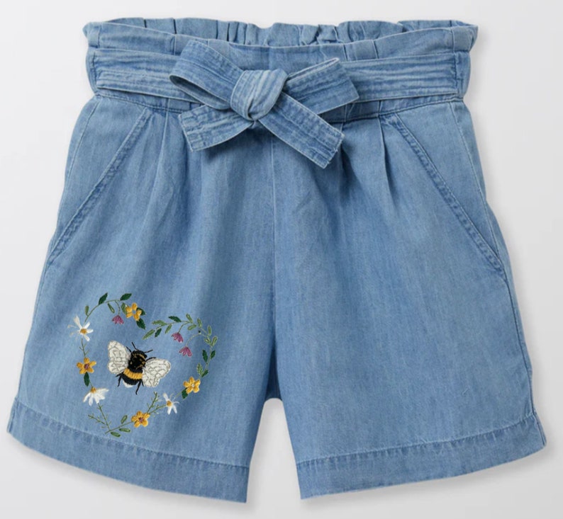 Peut inclure: Short en jean bleu clair &agrave; taille haute avec une ceinture &agrave; nouer. Le short est orn&eacute; d'un motif brod&eacute; en forme de c&oelig;ur avec une abeille et des fleurs.