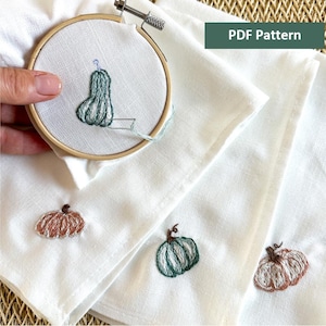 May include: Three white fabric napkins with embroidered pumpkins. One napkin features a green pumpkin, one features a brown pumpkin, and one features a green pumpkin with a stem.