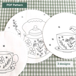 Könnte beinhalten: Drei Stickmuster für Tee-Motive. Die Muster zeigen eine Teekanne, eine Teetasse und eine Teetasse mit einem Vogel. Jedes Muster befindet sich auf einem weißen Kreis mit einem gepunkteten Rand.