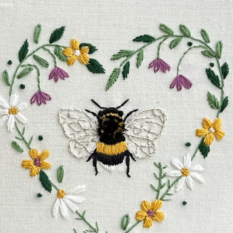 Peut inclure: Broderie repr&eacute;sentant un bourdon aux rayures jaunes et noires, entour&eacute; d'une couronne en forme de c&oelig;ur de fleurs blanches, jaunes et violettes.