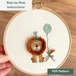 Peut inclure: Broderie d'un lion portant un chapeau de fête et tenant un ballon. Le lion est brun et beige avec un chapeau de fête vert et blanc et un ballon vert clair. Le texte "Step-by-Step Instructions" et "PDF Pattern" sont visibles.