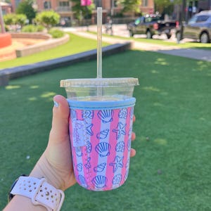 May include: A pink and blue insulated cup holder with a seashell and starfish pattern. The text "Beautifully You" is visible on the holder.