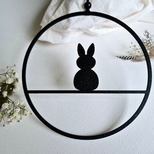 Könnte beinhalten: Schwarzer Metallring mit einer Silhouette eines Hasen, der von oben hängt. Der Hase sitzt auf einem kleinen Regal im Ring.