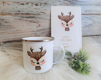 Könnte beinhalten: Weißer Emaillebecher und Grußkarte mit einer Aquarellillustration eines Rehs mit geschlossenen Augen. Auf der Karte steht in goldener Schrift "Happy Christmas for you". Der Becher hat einen silbernen Rand und Henkel.